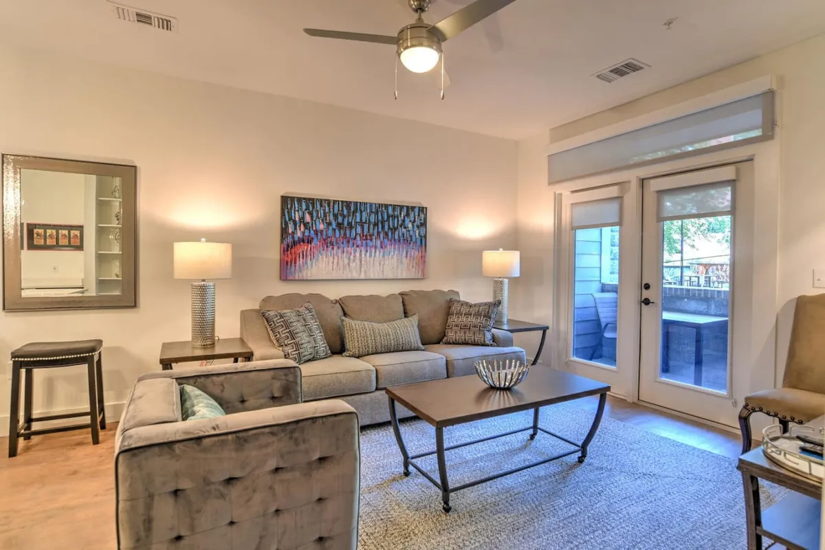 A cozy, sunlit living area with a plush sofa, stylish modern artwork, a chic coffee table, and warm lamplight creating an inviting space perfect for relaxing or socializing. The decor blends timeless elegance with artistic touches, reflecting the vibrant spirit of downtown Asheville.
