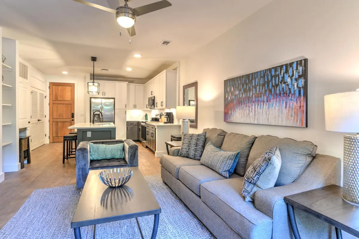 This image features a comfortable living area highlighted by a plush sofa and coffee table, with eye-catching artwork on the wall and a glimpse of the kitchen island in the background. The arrangement invites relaxation and socializing, embodying the cozy, urban-inspired atmosphere described in the section.