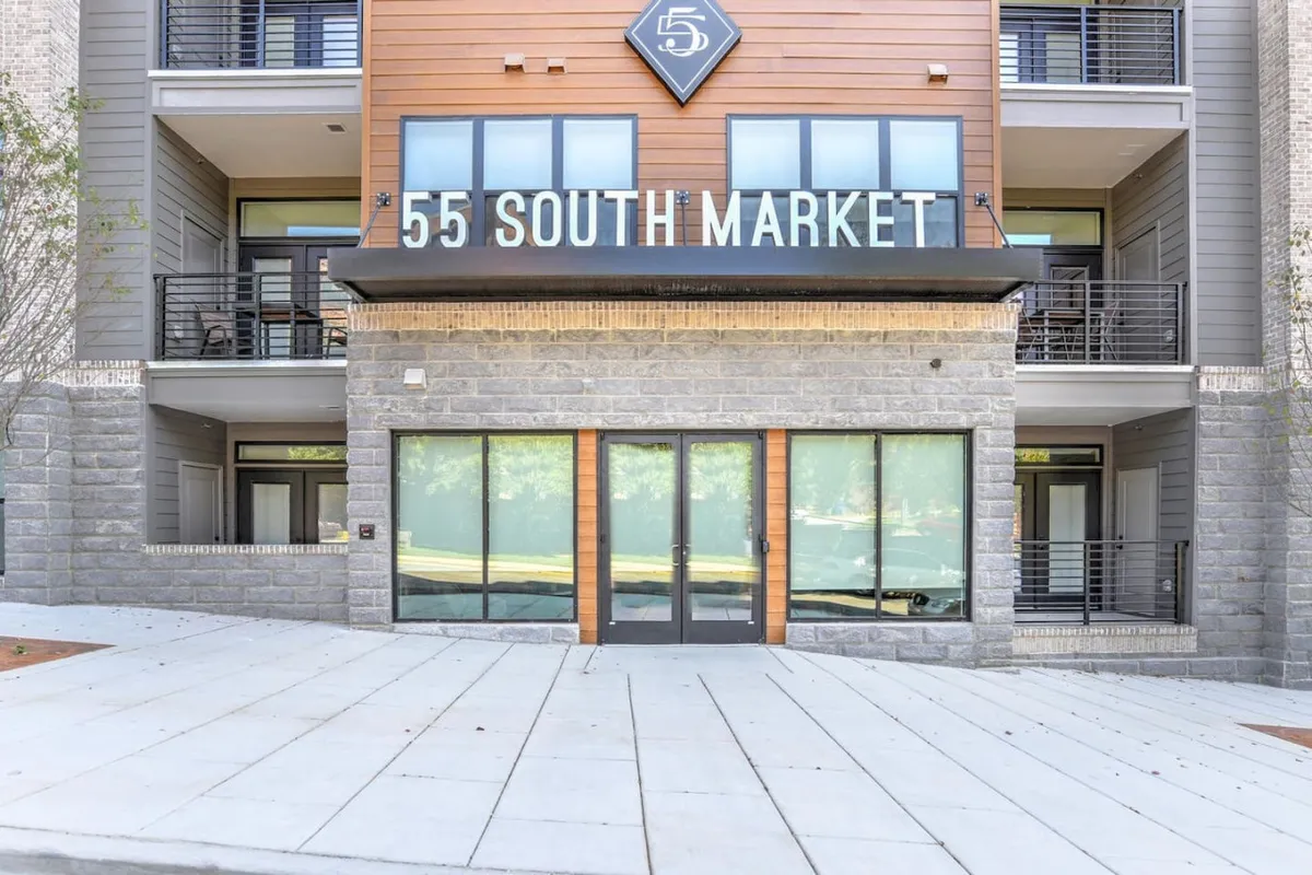 This image features the main entrance doors of the building, prominently displaying the '55 SOUTH MARKET' signage against a backdrop of modern architectural details. The setting is welcoming, hinting at both security and a sense of arrival directly from the street.