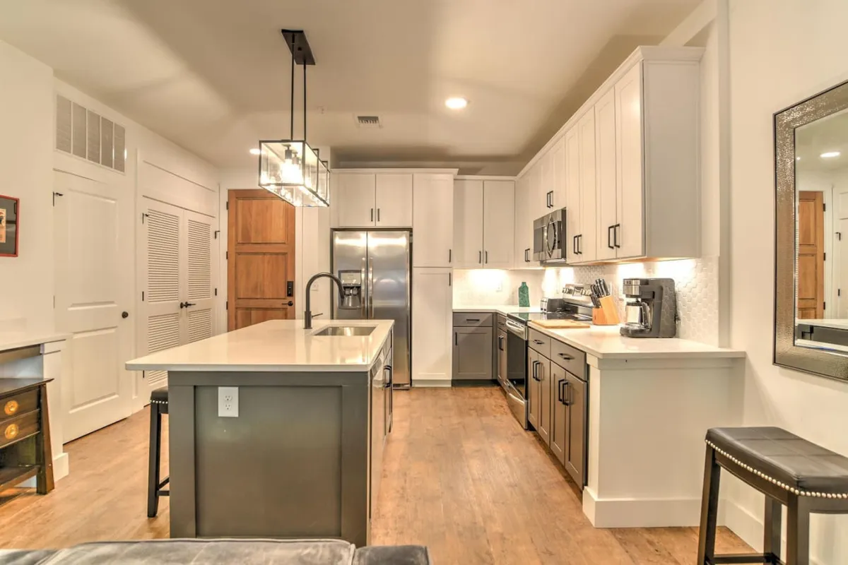 A cozy kitchen scene with an island countertop, stainless steel appliances, and neatly arranged cabinets. The setup is intimate and functional, ideally sized for preparing meals for two or sharing a quiet dinner. The warm lighting and compact design reinforce the idea of a chef’s nook and intimate dining experience.