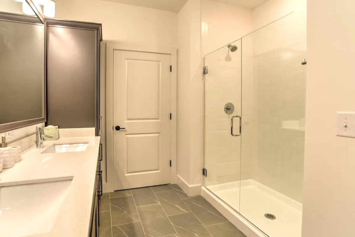 This photo showcases a modern bathroom with dual sinks, a sleek glass shower enclosure, and a large mirror. The space is bright and calm, designed for rejuvenating morning or evening routines, with contemporary finishes throughout.